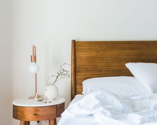 minimalist bedroom with wooden nightstand, lamp, wood headboard and white comforter
