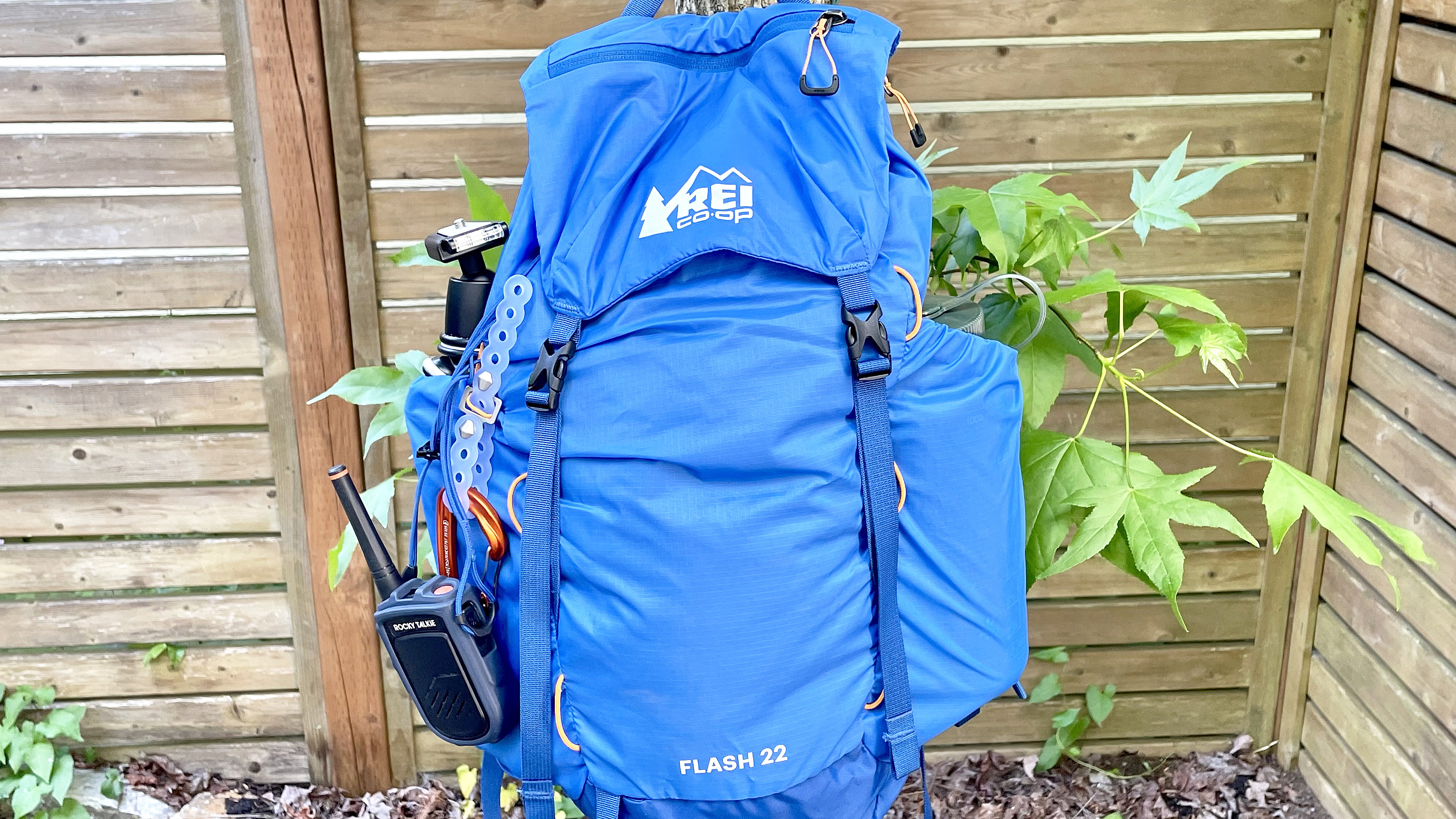 The REI Flash 22 pack in blue hanging from a tree branch and stuffed with gear