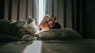 Woman lying back on bed with hand over face