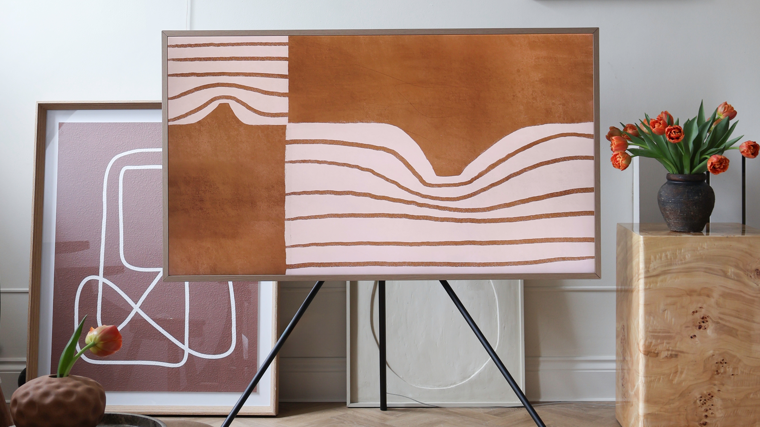 a frame TV on a stand in a room with artwork and a burl side table