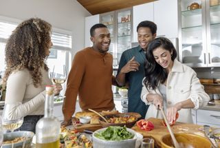 Woman in her 20s chopping bell peppers, preparing food at party with friends