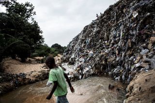 A young boy walking across a dirty river bank littered with garbage in 2017 in Kinshasa, Democratic Republic of the Congo.