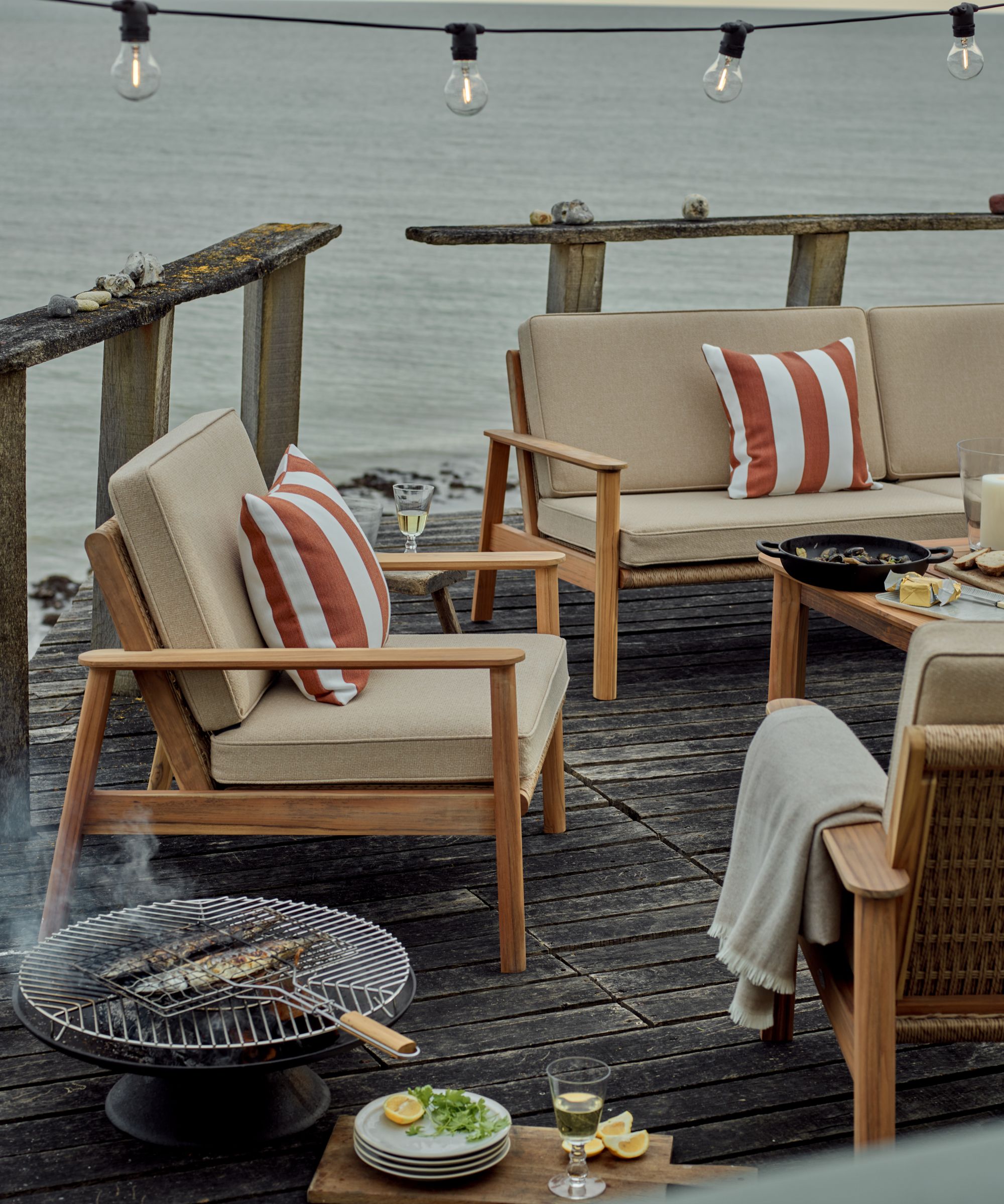 outdoor rustic lakeside wooden deck patio with teak patio sofas with orange and white striped pillows and an outdoor grill