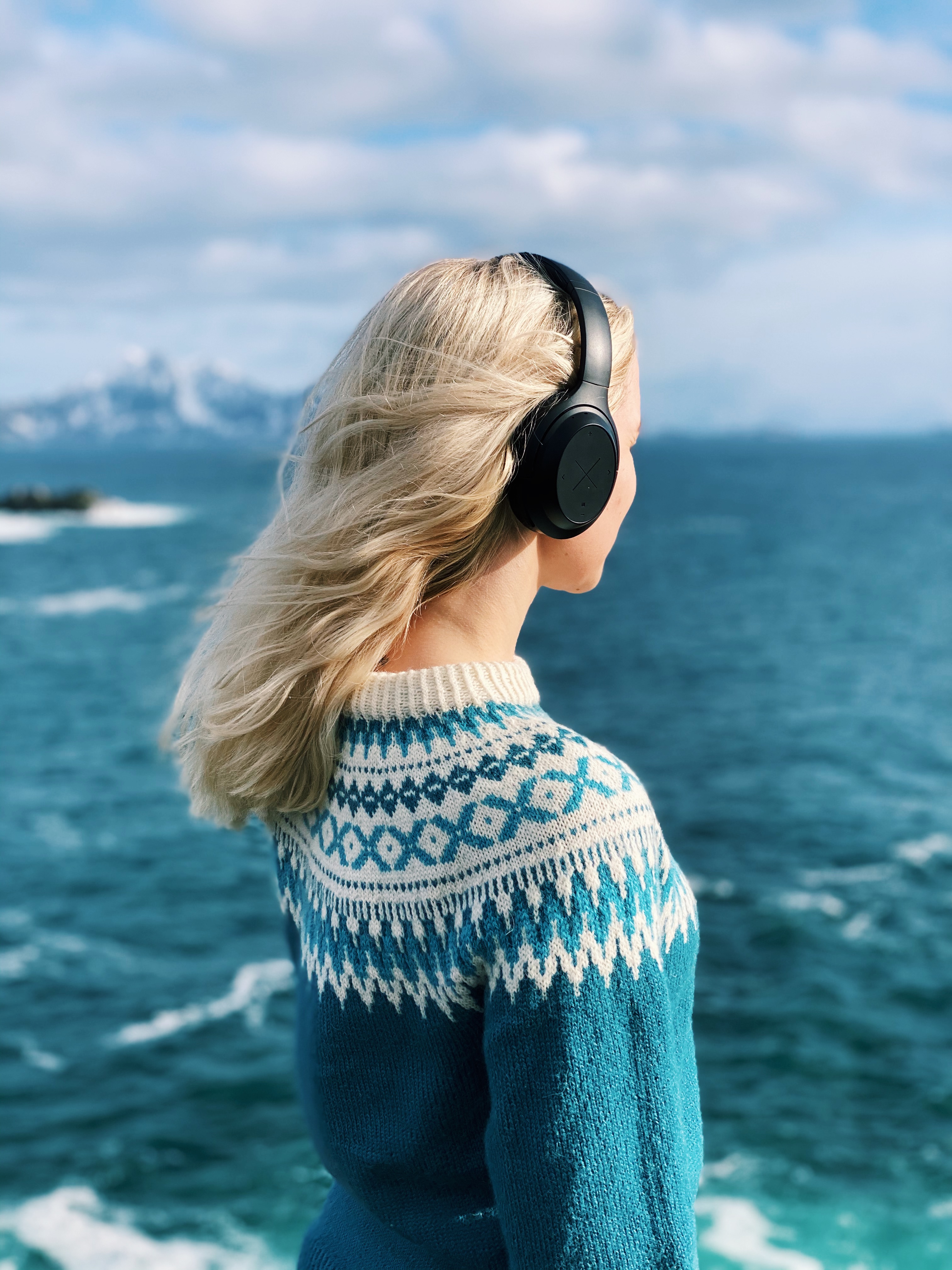 X by Kygo A11/800 -kuulokkeet naisen päässä meren rannassa
