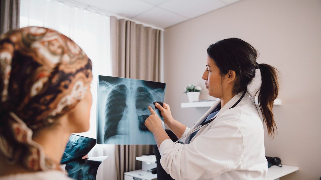 Female doctor talking to female cancer patient while examining x-ray in doctor&#039;s office