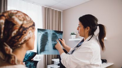 Female doctor talking to female cancer patient while examining x-ray in doctor's office