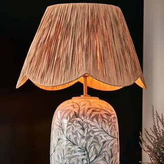 A close up shot of a table lamp with a willow shade and floral base shot against a black background