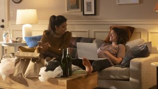 Sitting on a couch with beer and Chinese food around them, are (L-R): Ginger Gonzaga as Nikki Ramos and Tatiana Maslany as She-Hulk/Jennifer "Jen" Walters in Marvel Studios' She-Hulk: Attorney At Law