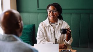 Woman holding cup of coffee sitting at table with man, laptop on table, smiling and laughing