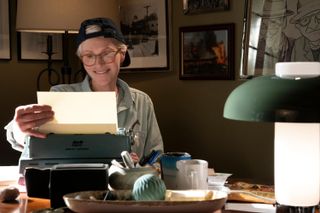 Jane Lynch as Sazz Pataki, smiling as she sits at a desk and takes a sheet of paper out of a typewriter, in 'Only Murders in the Building' season 4.