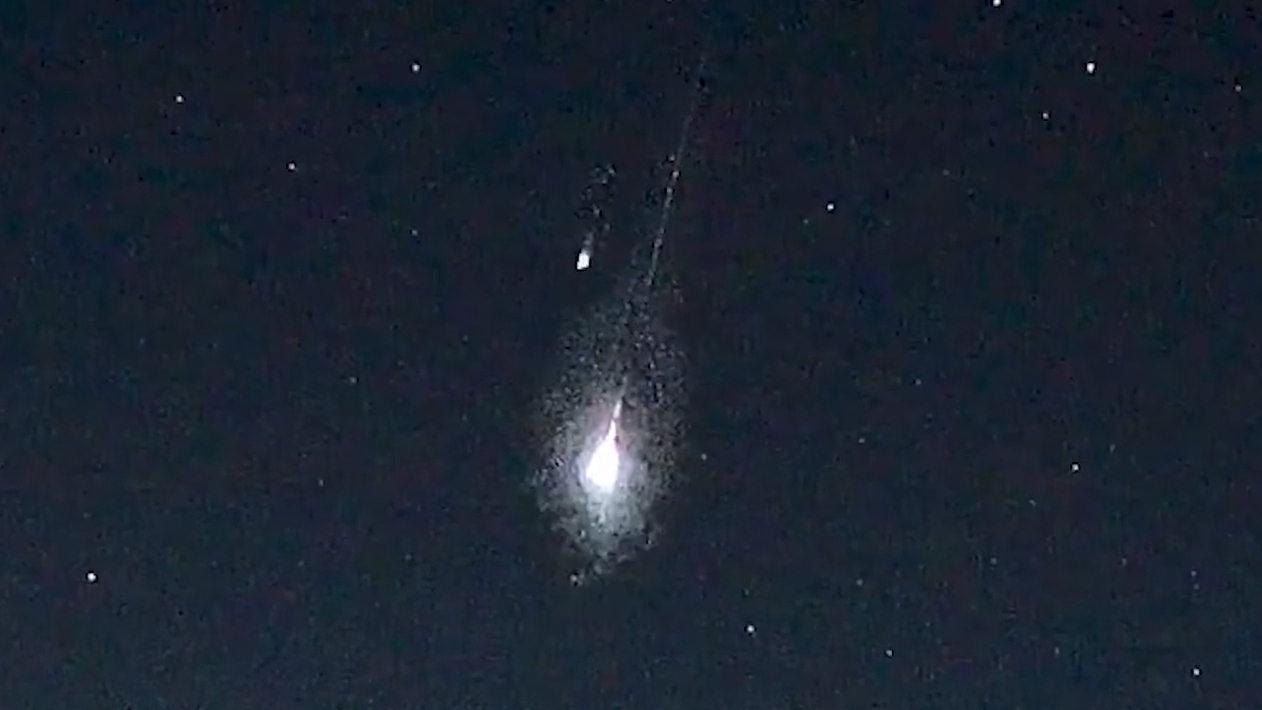 Two meteors are pictured streaking Earthward through a black sky peppered with white stars.