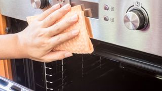 person cleaning the outside of the oven with a damp cloth