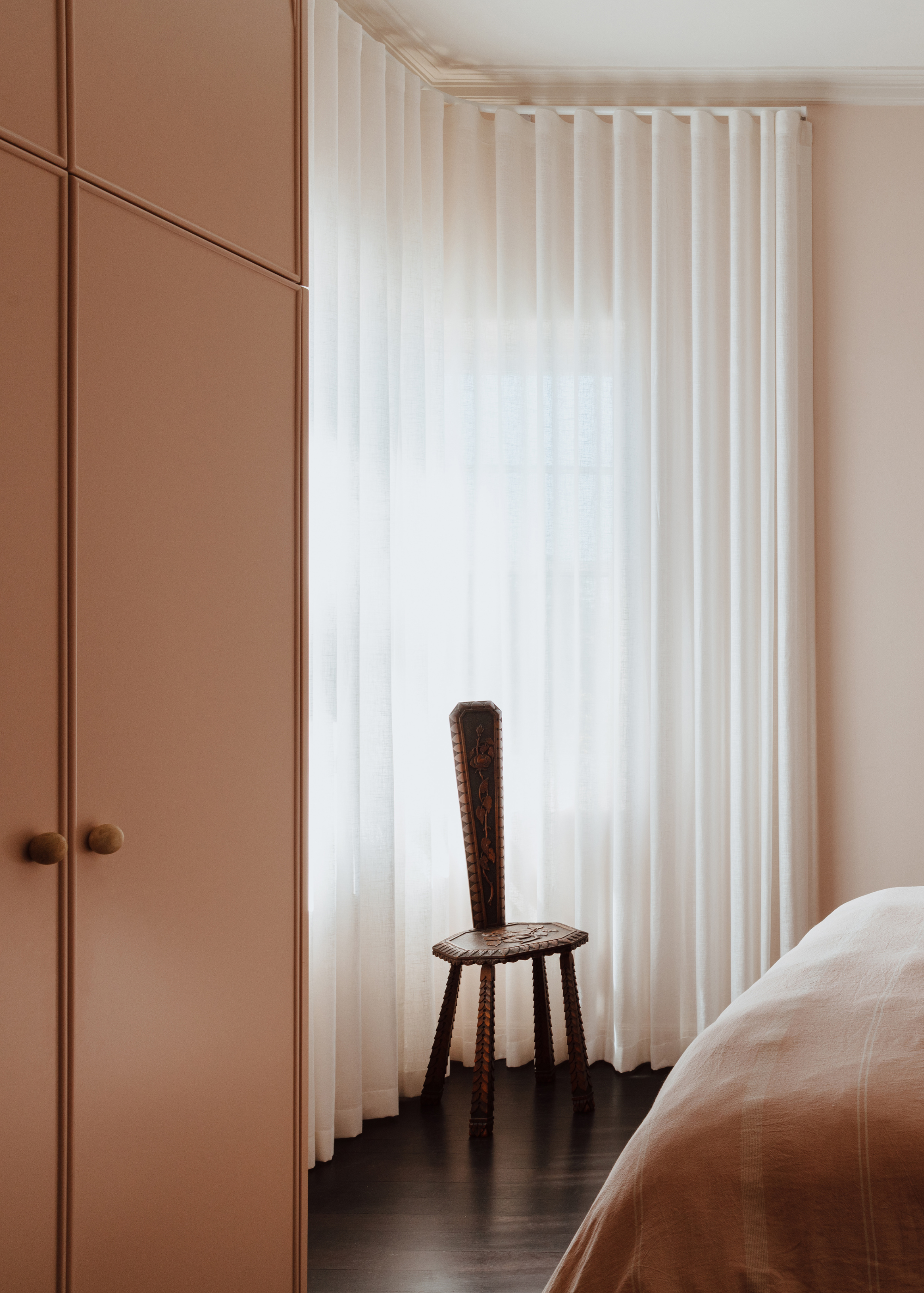A light pink bedroom with plush pink wardrobes and a wooden chair
