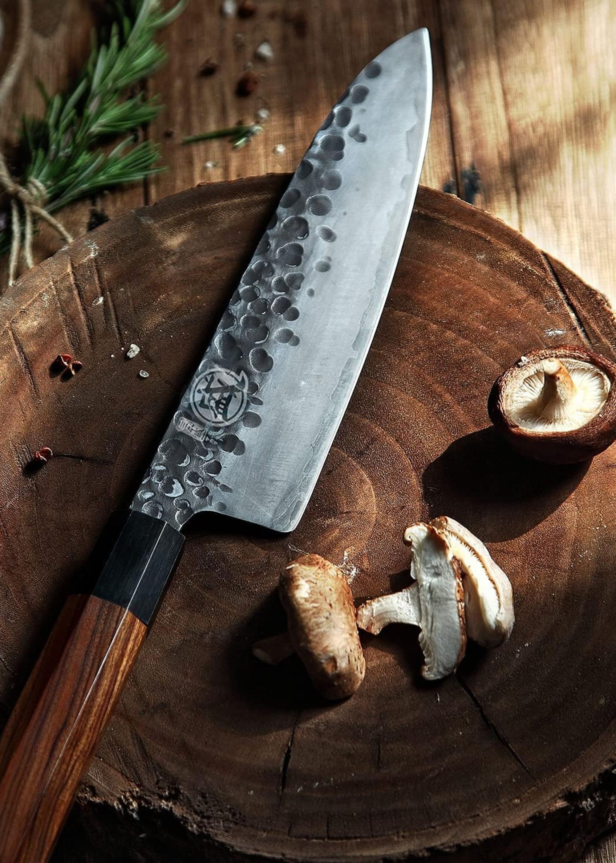 A Japanese knife from MITSUMOTO SAKARI on a wood chopping block beside rosemary and mushrooms
