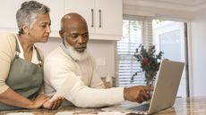 An older couple have a serious discussion while looking at a laptop in their kitchen.