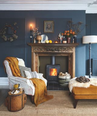 Dark living room with autumnal fireplace, ochre footstool, cream armchair and ochre throw