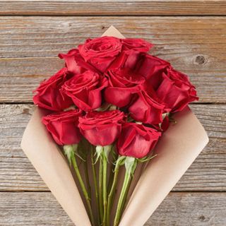 A dozen red roses wrapped in paper on a brown table