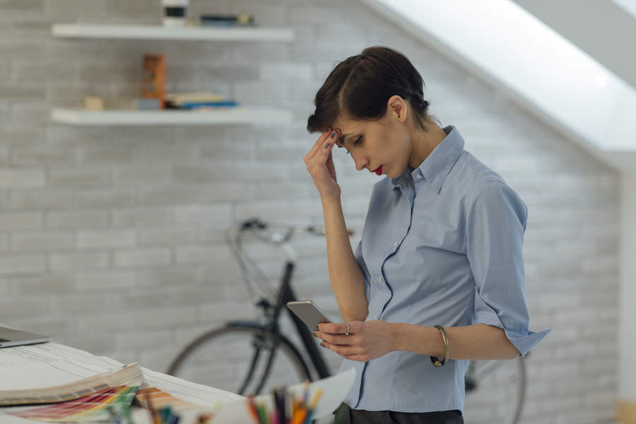 Young Female architect working in her office. She is under pressure. She received bad news on message on her smart phone.