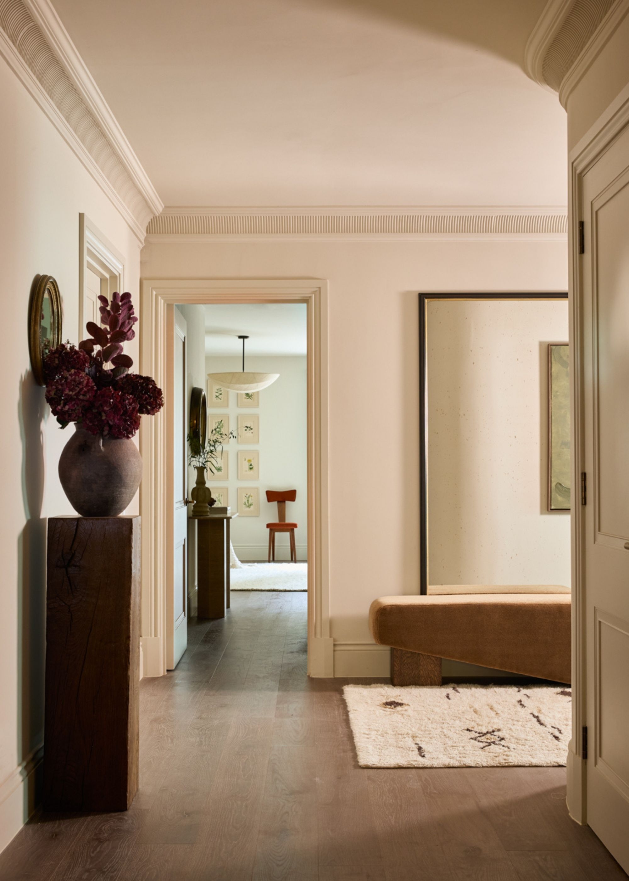A large and traditional room with modern and minimal decor, including warm white walls, dark wooden vintage furniture, a textured rug, and a large mirror.