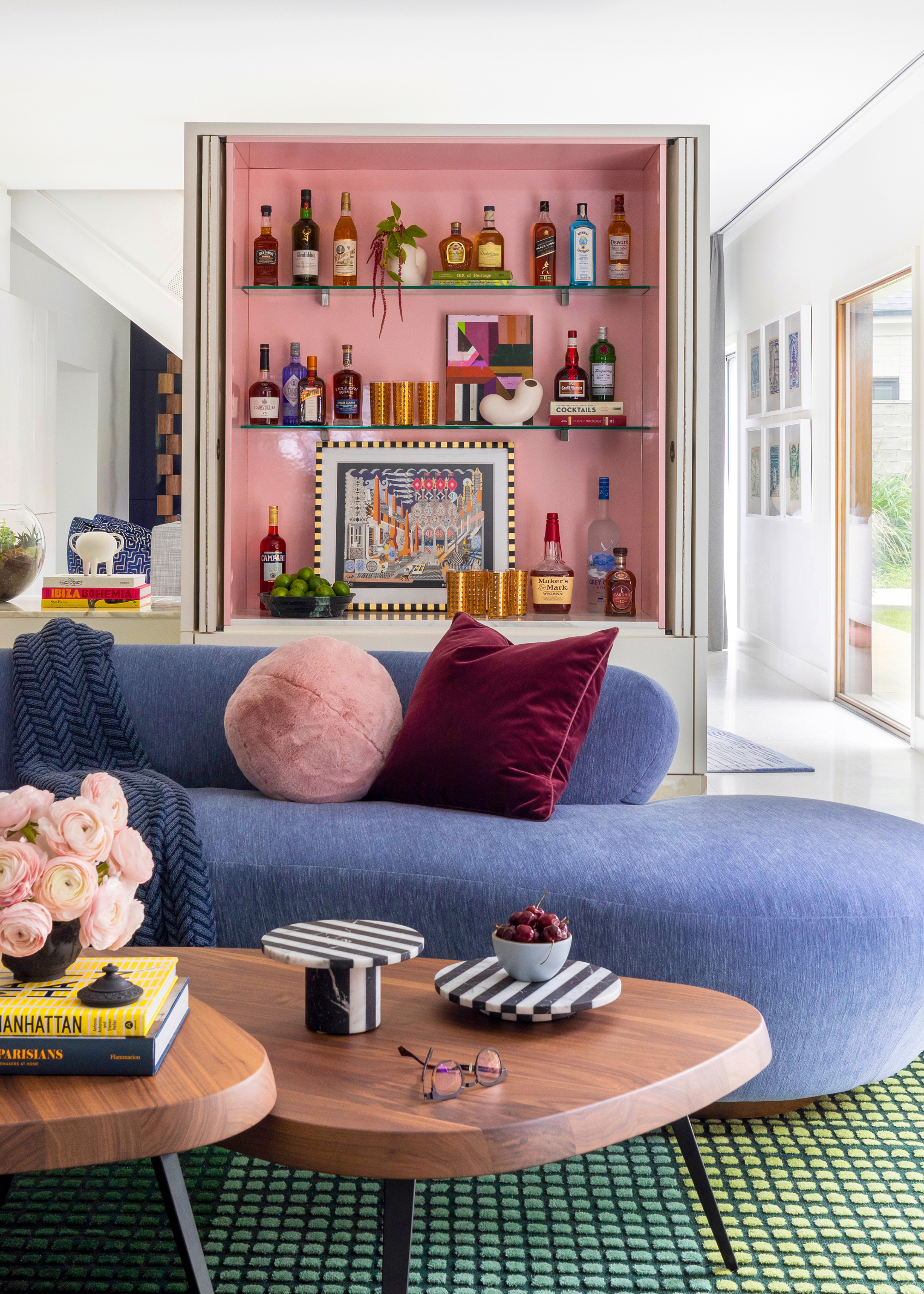 a living room with a home bar with a pink backed unit on display in the center of the room with a blue sofa in front with blankets and cushions on it