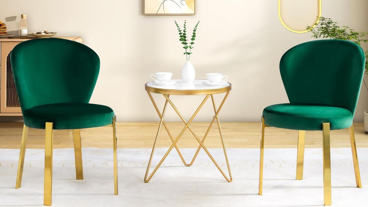 The best Amazon furniture brands and finds are easy to shop. Here is a living area with two dark green and gold velvet seats, a white gold side table, a white rug underneath these and a beige wall behind them