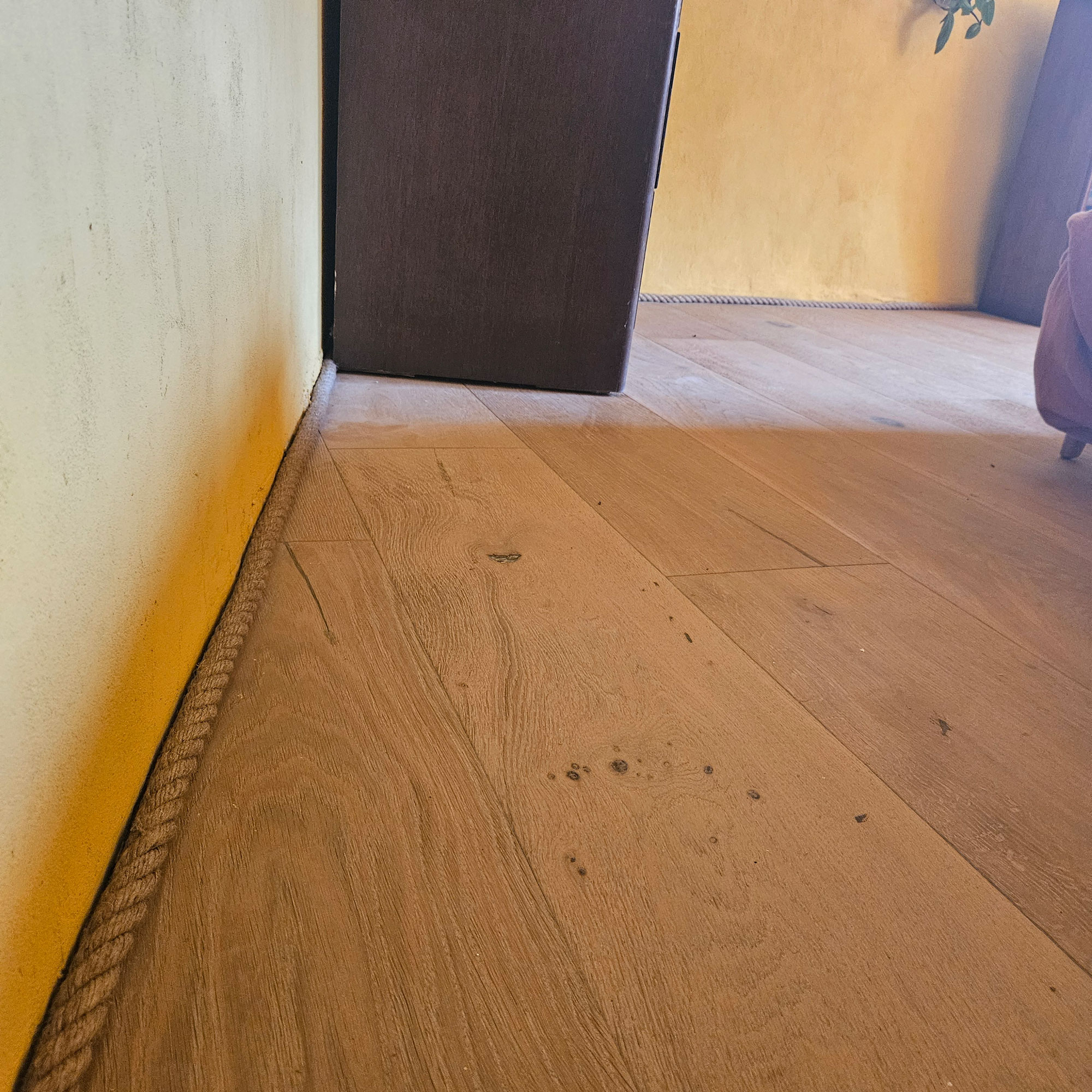 Yellow limewashed room with rope skirting board and brown wood furniture