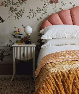 An example of bed ideas showing a bed with a scalloped pink headboard and floral wallpaper