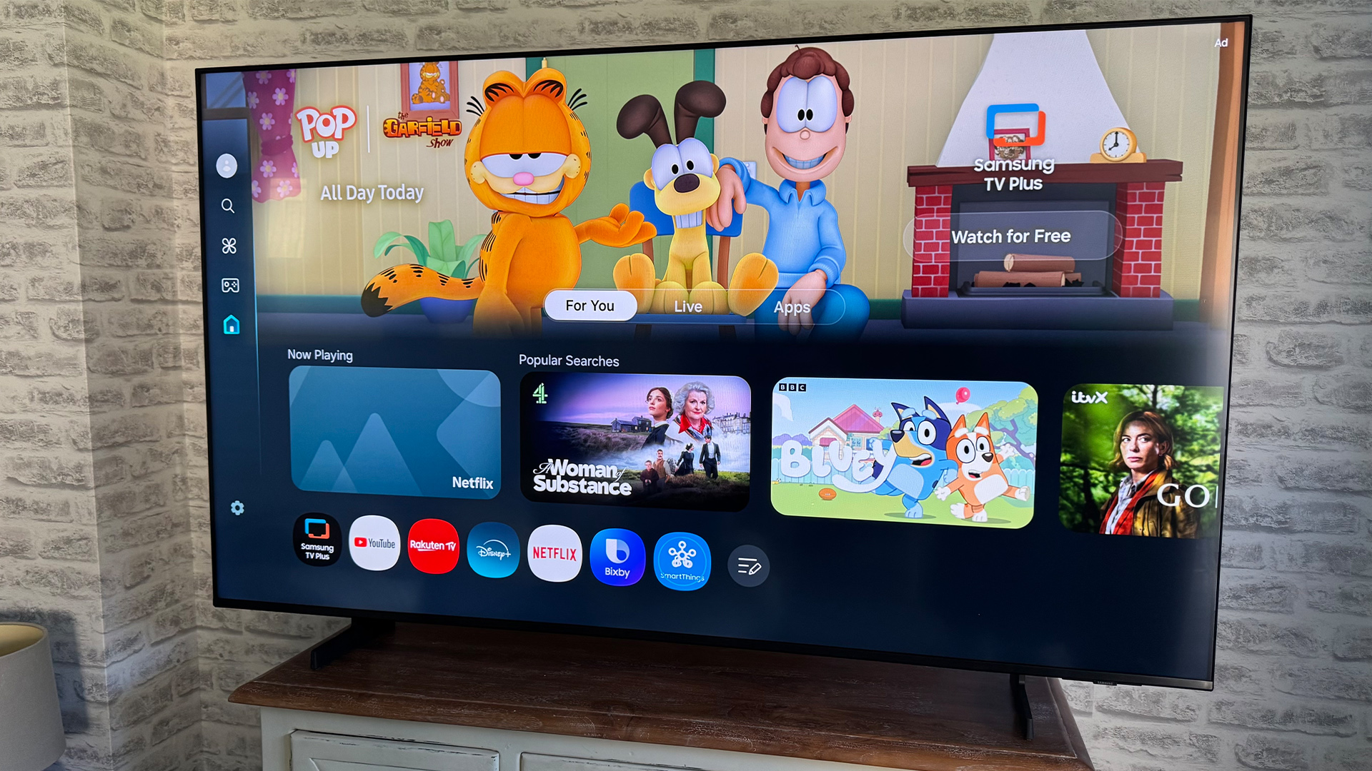 Samsung UE65U8000F 65-inch TV on wooden sideboard in front of brick wall, on screen is Tizen OS