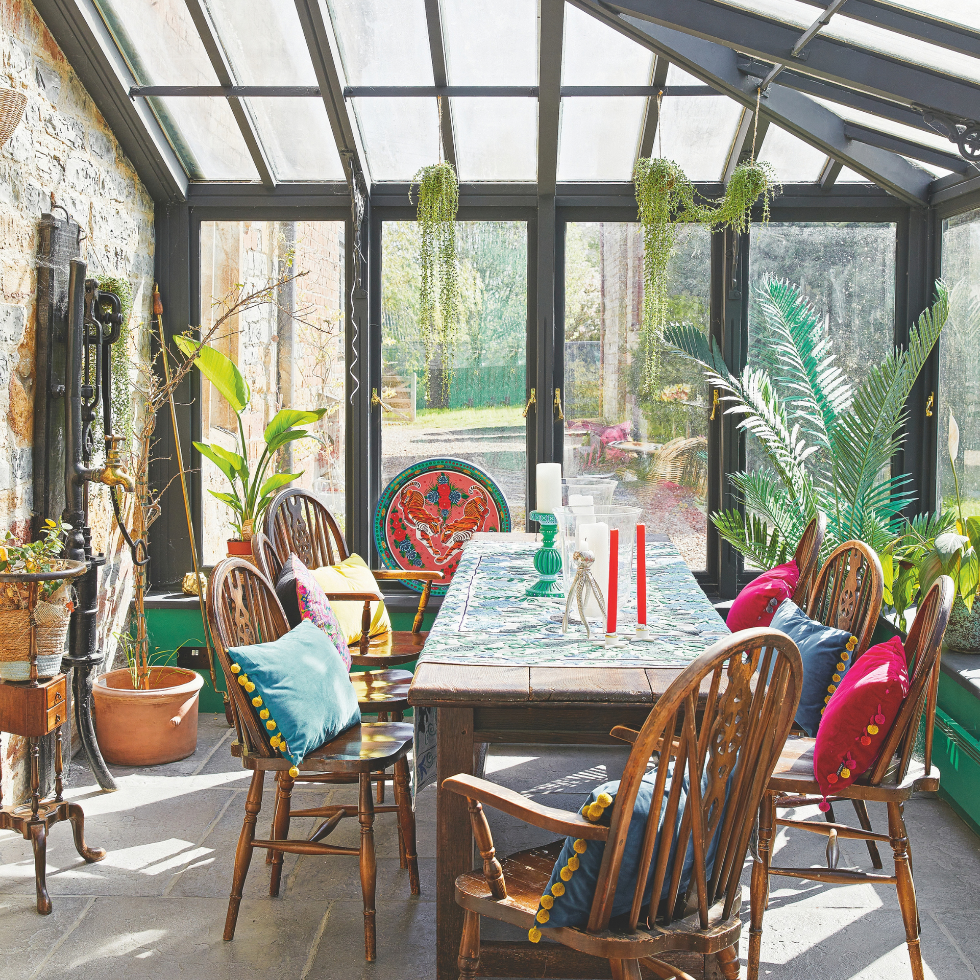 Wooden dinging table and chairs with colourful accessories in a conservatory.