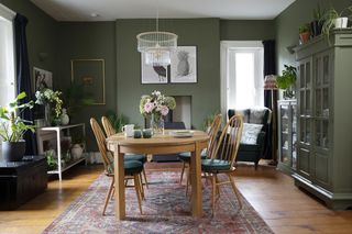 Dining room with green walls, burgundy Persian rug, chandelier over wooden dining table and chairs, and green painted dresser