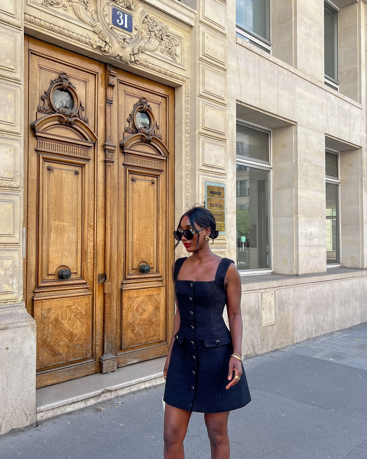 @aidabadji_ wearing a little black dress and a low bun with loose strands of hair framing her face