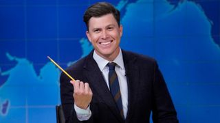 Colin Jost smiles and holds a pencil during Weekend Update on Saturday Night Live.