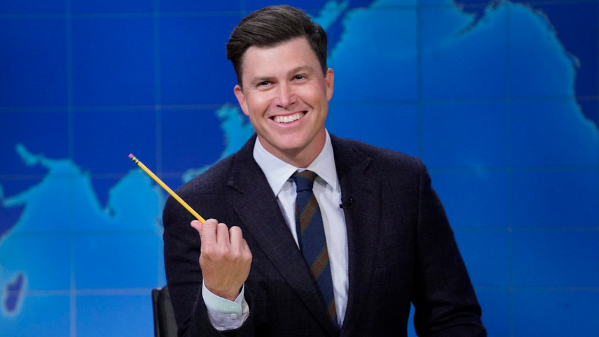 Colin Jost smiles and holds a pencil during Weekend Update on Saturday Night Live.