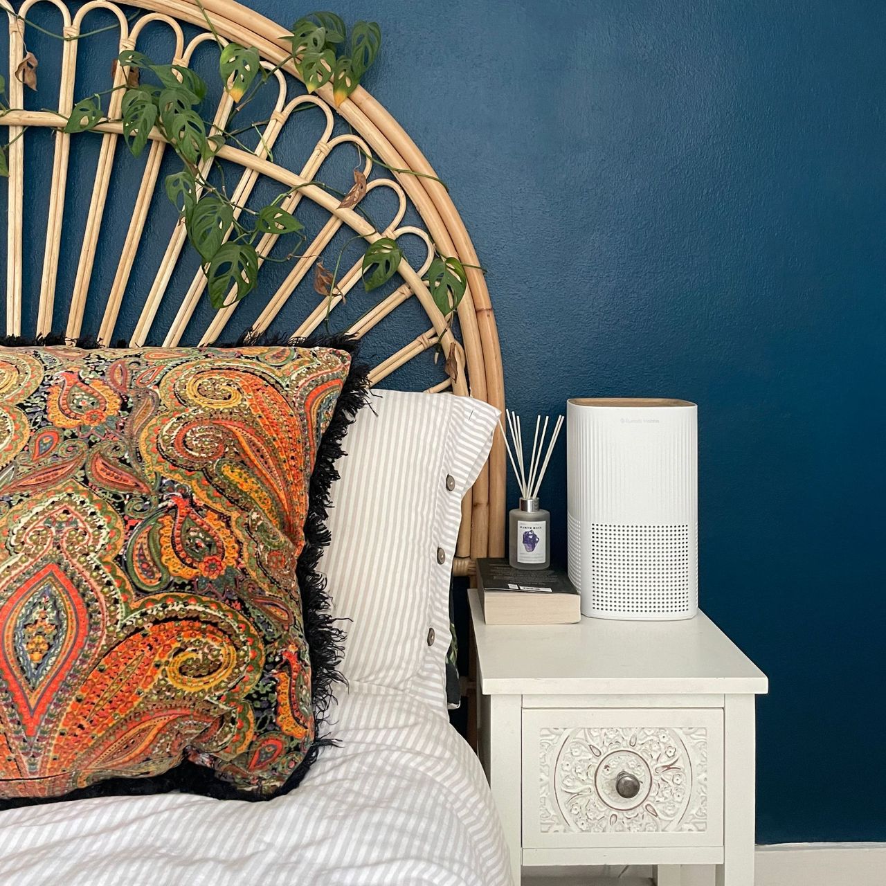 Russell Hobbs bedroom air purifier on a bedside table, next to a bed with striped bedding and a wooden bed frame