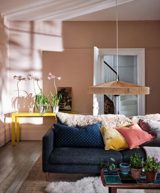 pastel living room ideas, pastel living room with pink walls, yellow console, denim style couch, low pendant light, sheepskin on couch, cushions