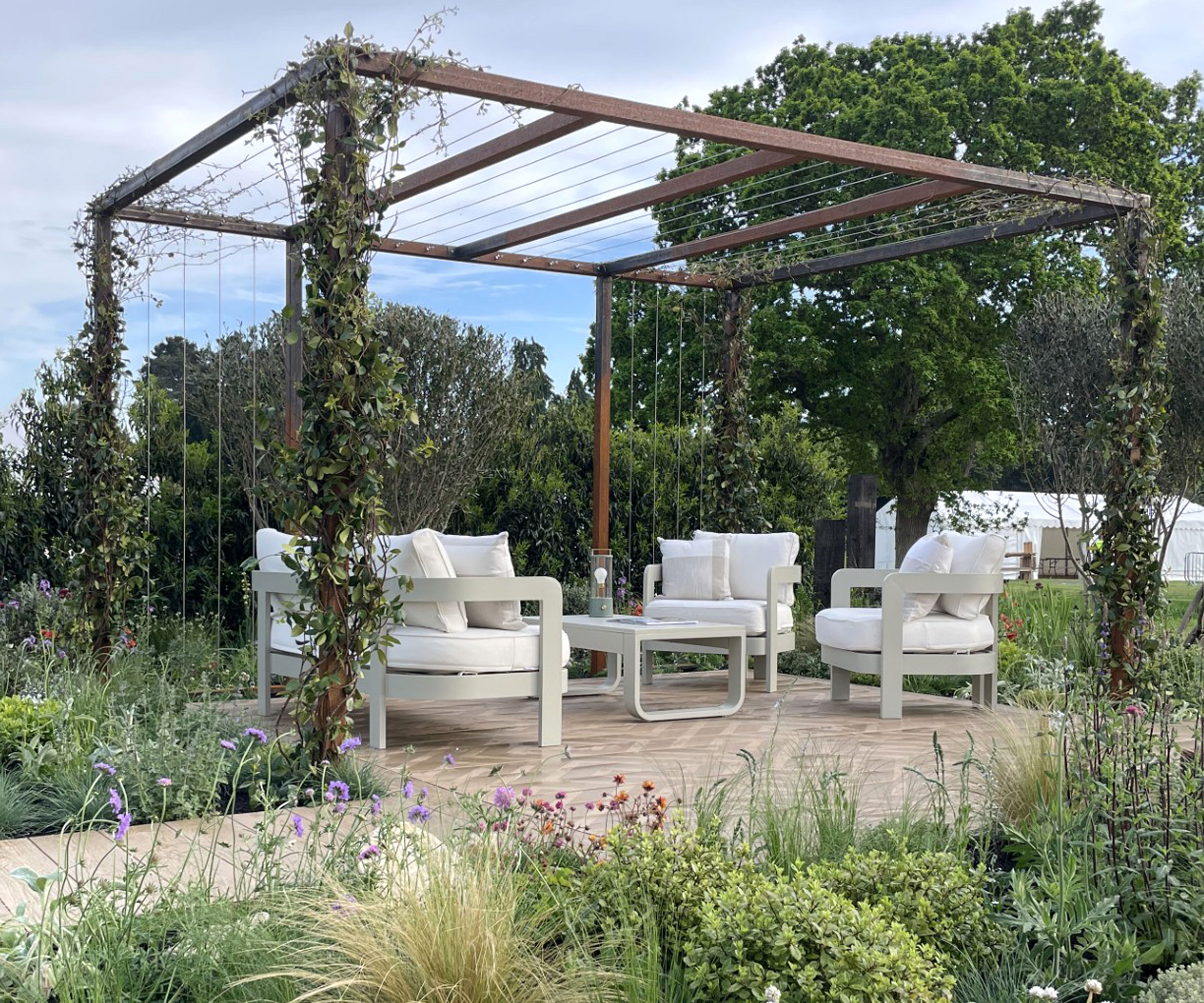 corten metal pergola with climbing plants, garden furniture on patio, and planted flowerbeds around