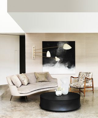 A neutral living room with silk and velvet sofa and round black coffee table.