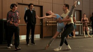 Tobias (Gideon Glick) and Jack (Luke Kirby) looking at two dancers, a man is holding a woman who is lifting her leg above his head. 