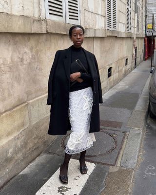 Fashion influencer Sylvie Mus on the street in Paris wearing a chic fall outfit styled with a white skirt.