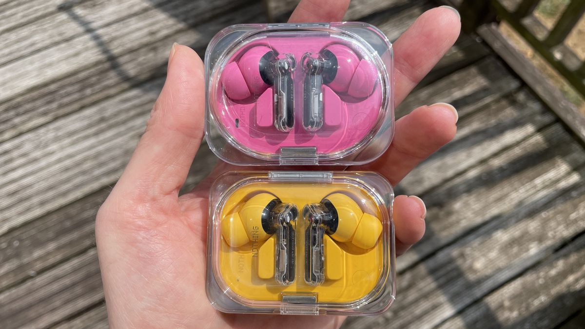 Nothing Ear (3a) in pink and Nothing Ear (a) in yellow, held in a hand and on beige background