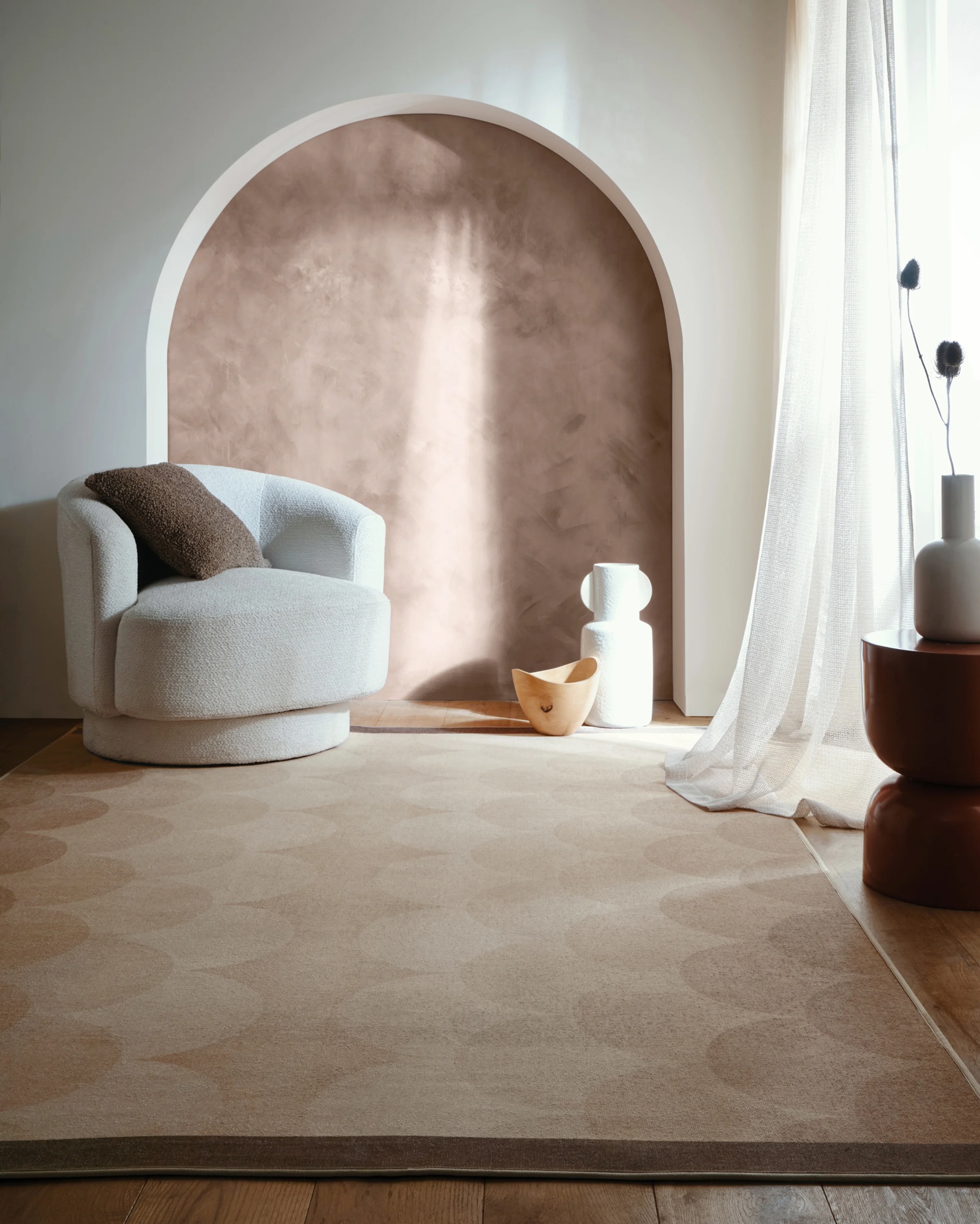 Hug Rug x Livingetc scallop ombre rug with white armchair, sheer drapes, and alcove with terracotta limewash, and sculptural decor on floor