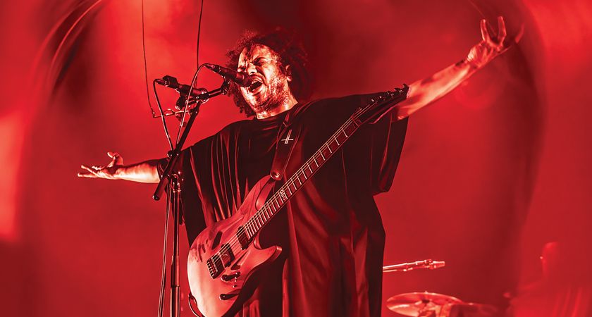 Manuel Gagneux of Zeal &amp; Ardor pictured onstage, arms outstretched with his Aristides electric guitar, on a stage light in red