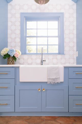 Kitchen with blue cabinets, sink and faucet, window, and tile backsplash