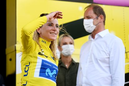 Annemiek van Vleuten blocks sun from her eyes as she smiles. Christian Prudhomme and Marion Rousse stand blurred in the background. 