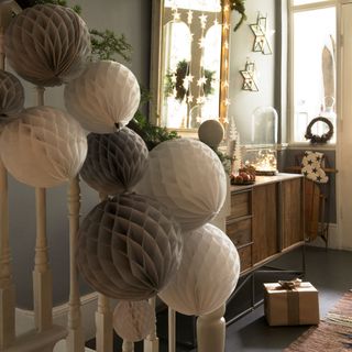 Neutral cream and brown paper lanterns tied to white staircase next to wrapped box on floor