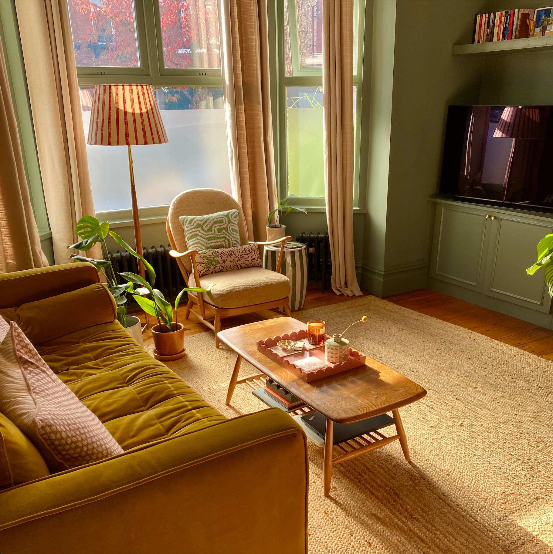 Green living room with jute rug, wooden coffee table, velvet sofa and wooden armed armchair