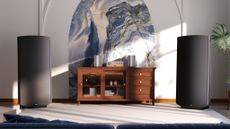 A pair of Quad ESL 2912X speakers in a brightly lit room on either side of a wooden sideboard with Quad audio components on top of it