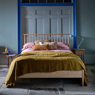 A dark blue bedroom with a wooden bedframe dressed in mustard and pink bedlinen