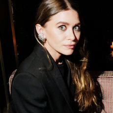 a brunette Ashley Olsen at an event wearing statement earrings and a black blazer