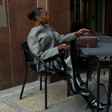 influencer sits down while wearing a gray blazer and long knee high black boots while wearing gold jewelry